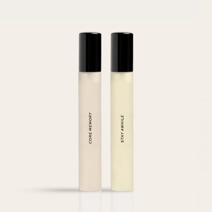 Two cylindrical fragrance bottles with black caps labeled "Core Memory" and "Stay Awhile" in cream and pale yellow liquid.