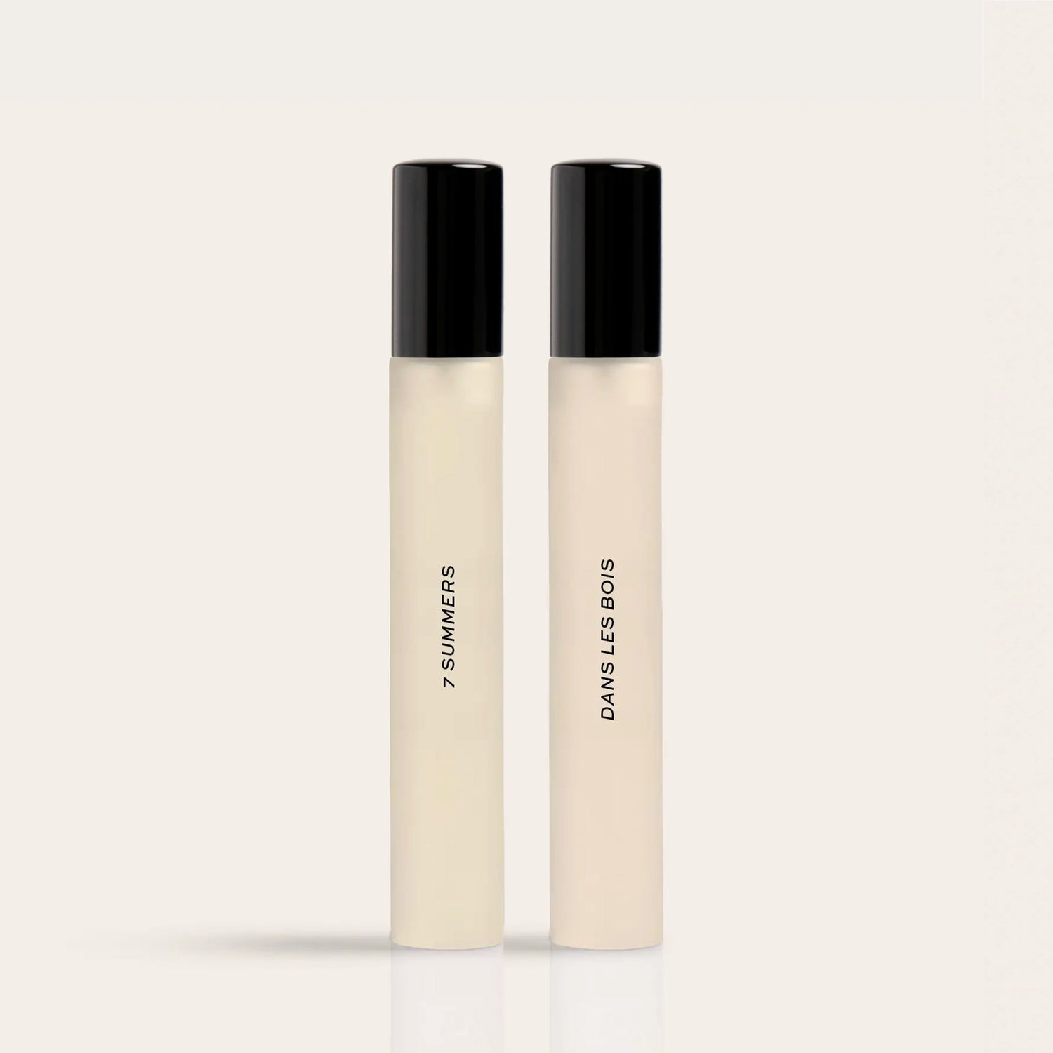 Two cylindrical fragrance bottles with black caps and cream-colored liquid, labeled "7 Summers" and "Damselless Bodies".