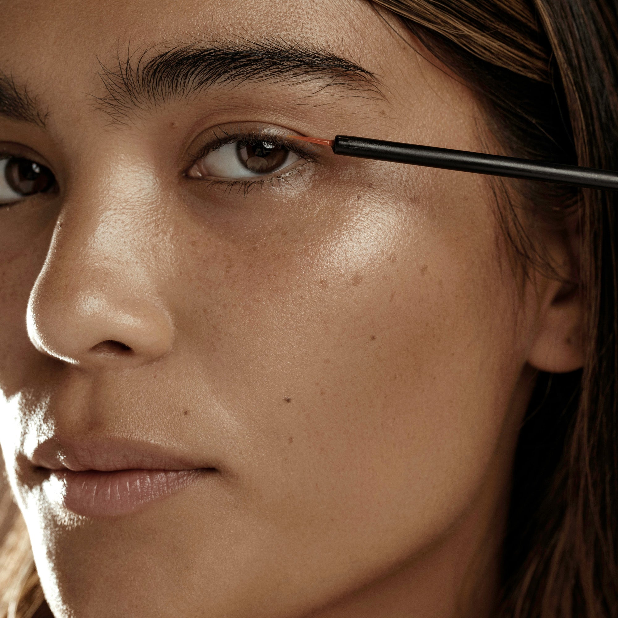 a woman applying makeup with a pencil on her eyebrow