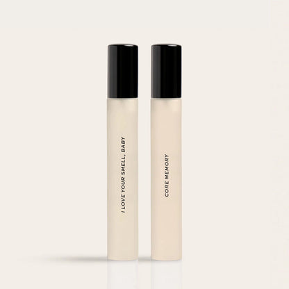 Two cream-colored fragrance rollerballs with black caps labeled "I Love Your Smell Baby" and "Core Memory".