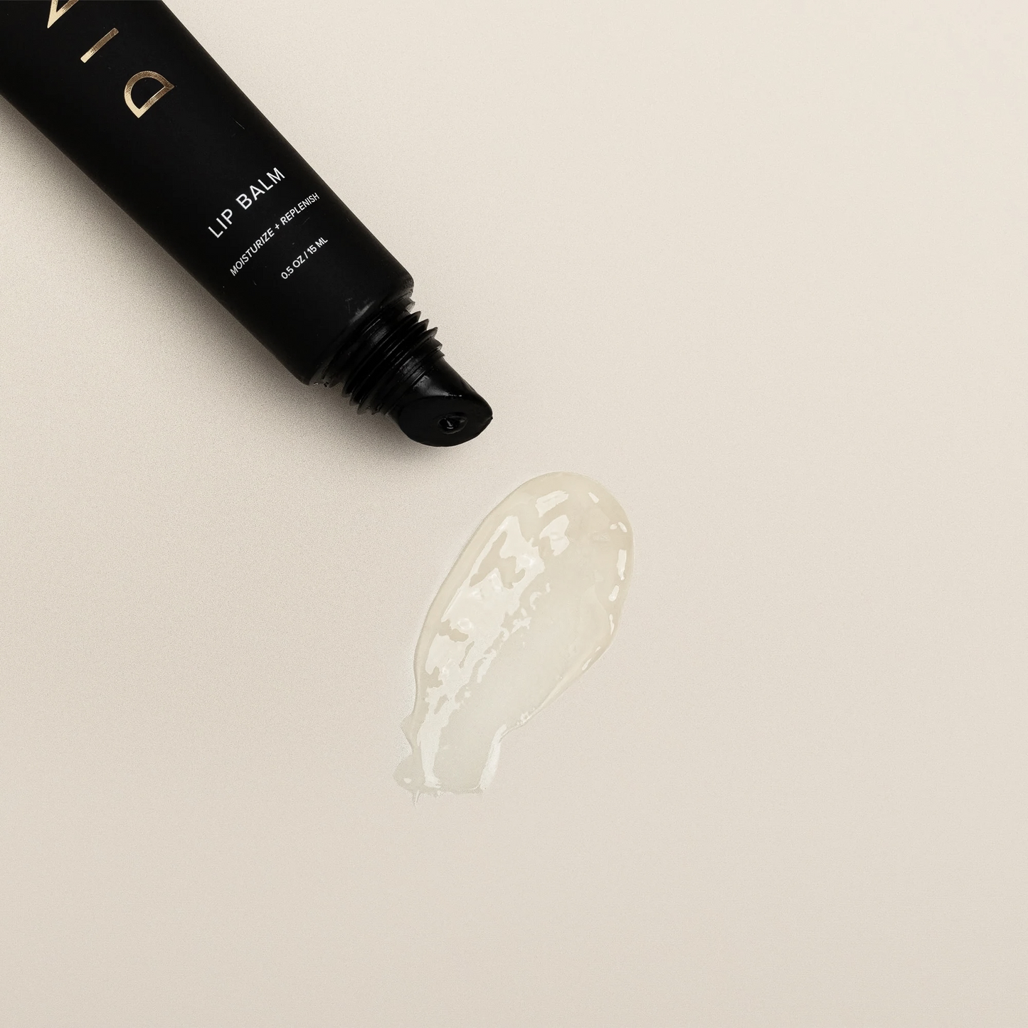 Black lip balm tube with white text label and clear gel swatch below on cream background.