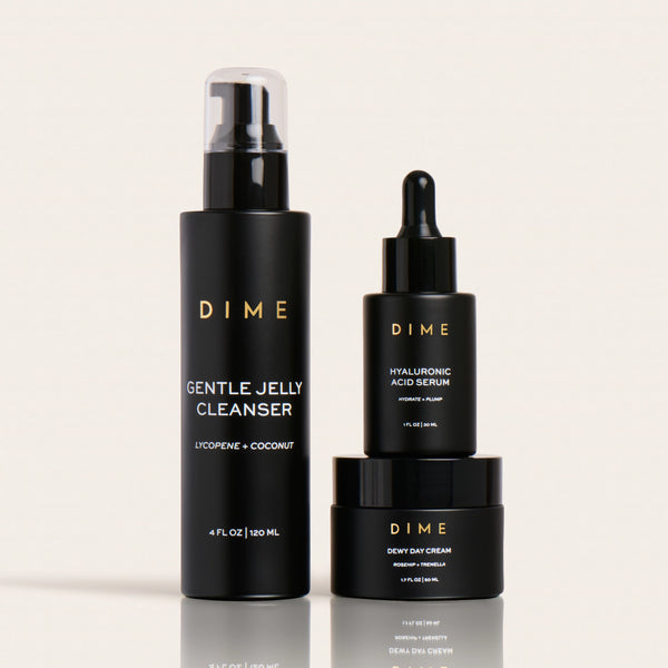 Three black DIME skincare bottles: Gentle Jelly Cleanser spray, Hyaluronic Acid Serum dropper, and Dewy Day Cream jar.