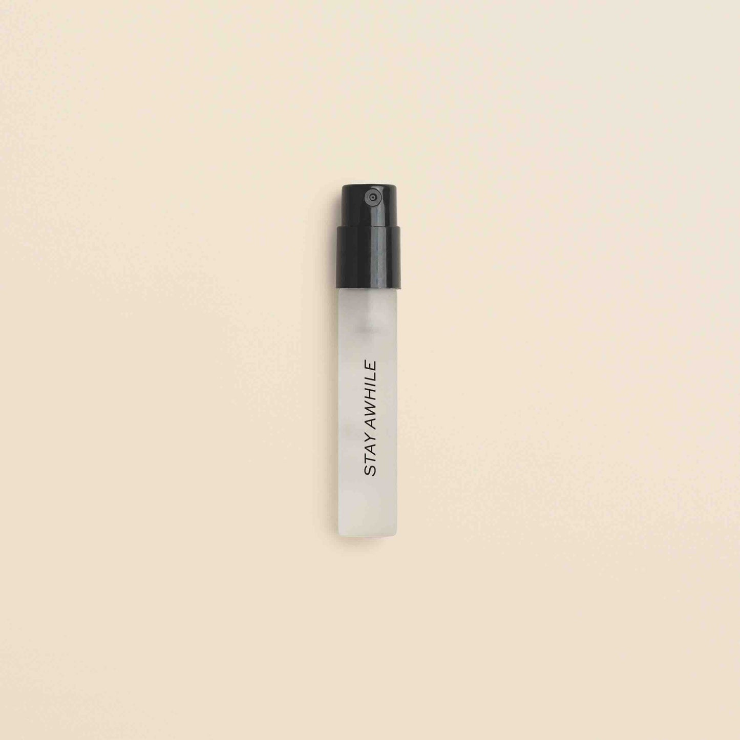 Small frosted glass spray vial with black atomizer top labeled "Stay Awhile" on beige background.